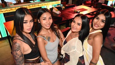DZ6_2010: Four friends enjoying a night out, smiling together at the camera in a lively bar setting.